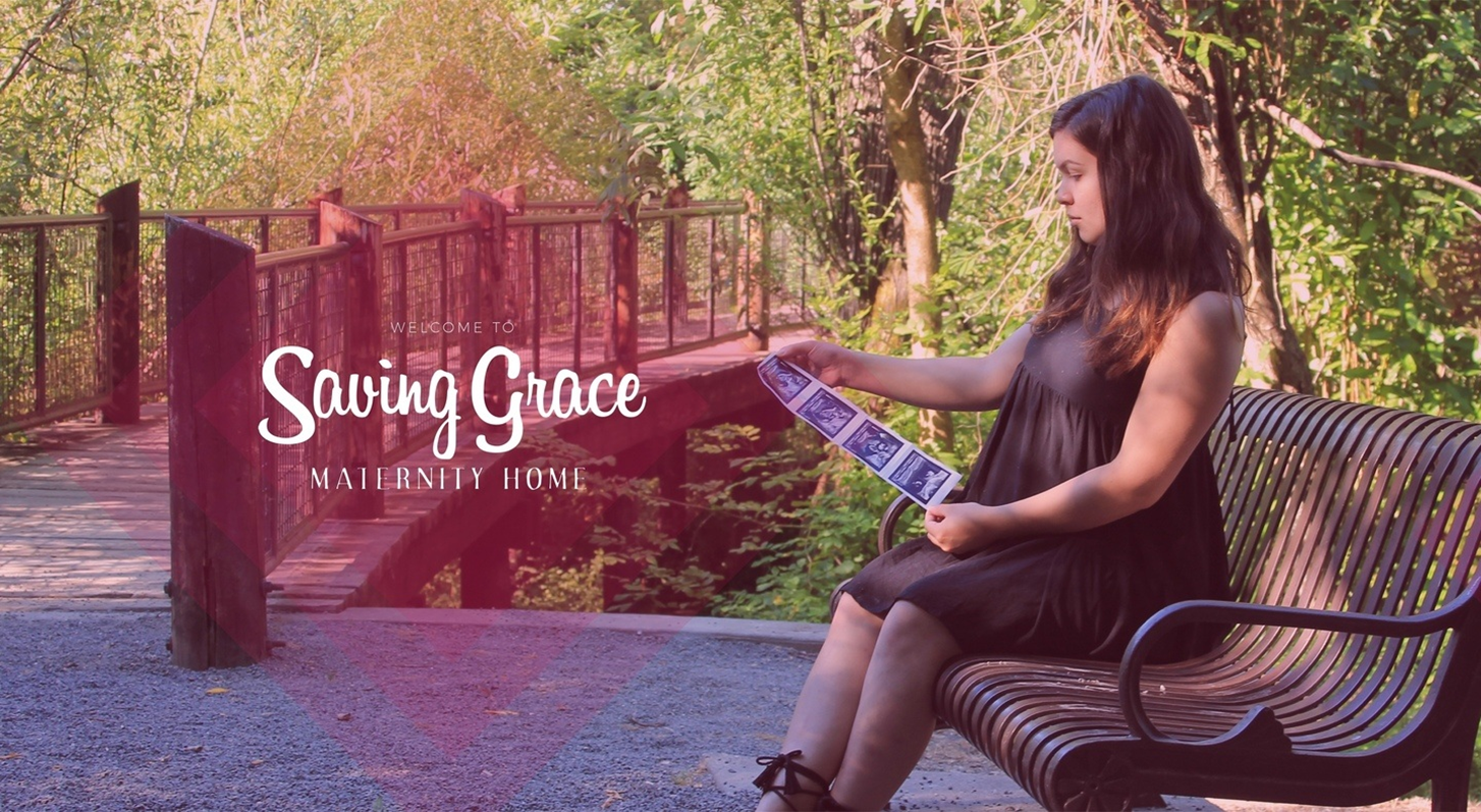 A woman looks at ultrasound pictures while sitting on a park bench near a bridge and the words "Saving Grace Maternity Home".